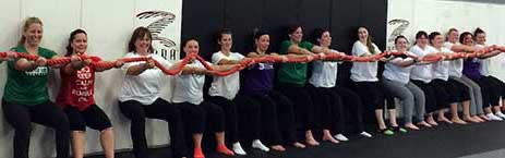 A line of Battle Girl members holding a wall sit together.