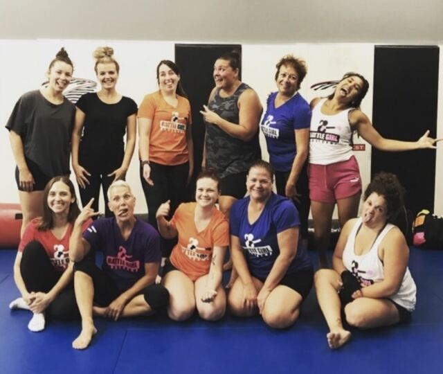 A group of Battle Girl Bootcamp members in their Battle Girl shirts, posing together on the blue mats.