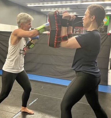 Two women working pad rounds in a Battle Girl Bootcamp class at Rumble Martial Arts in Keswick, one throwing a punch into a Thai pad her partner is holding.