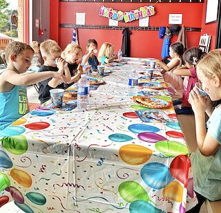 Kids sharing pizza and drinks at a long table under a Happy Birthday banner at a Rumble birthday party.