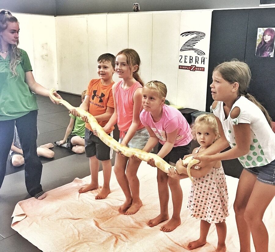 Kids and a handler holding a long pet python together on the mats at Rumble Martial Arts.