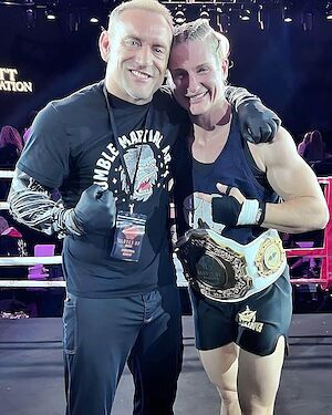Coach Jones in the ring with one of his fighters holding her championship belt.