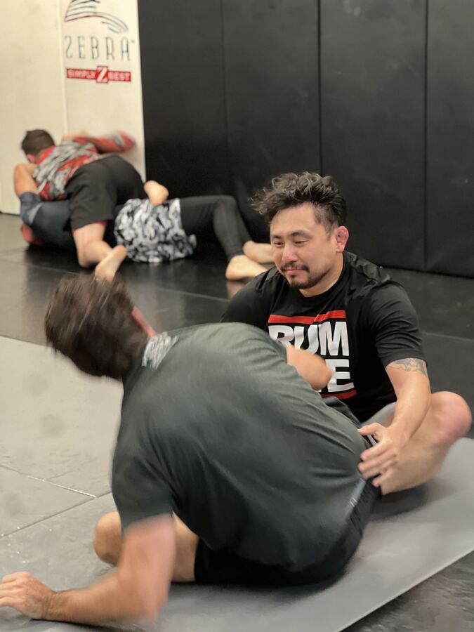 Two Rumble members drilling No-Gi BJJ on the mats, a coach guiding them.
