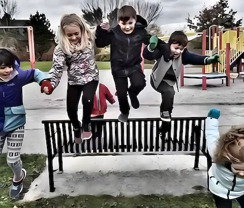 After-school kids jumping off a bench on a park outing.