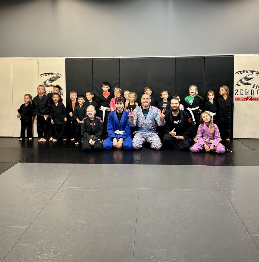 A Tiny Ninjas jiu-jitsu class and their coaches smiling on the mats at Rumble Martial Arts in Keswick.